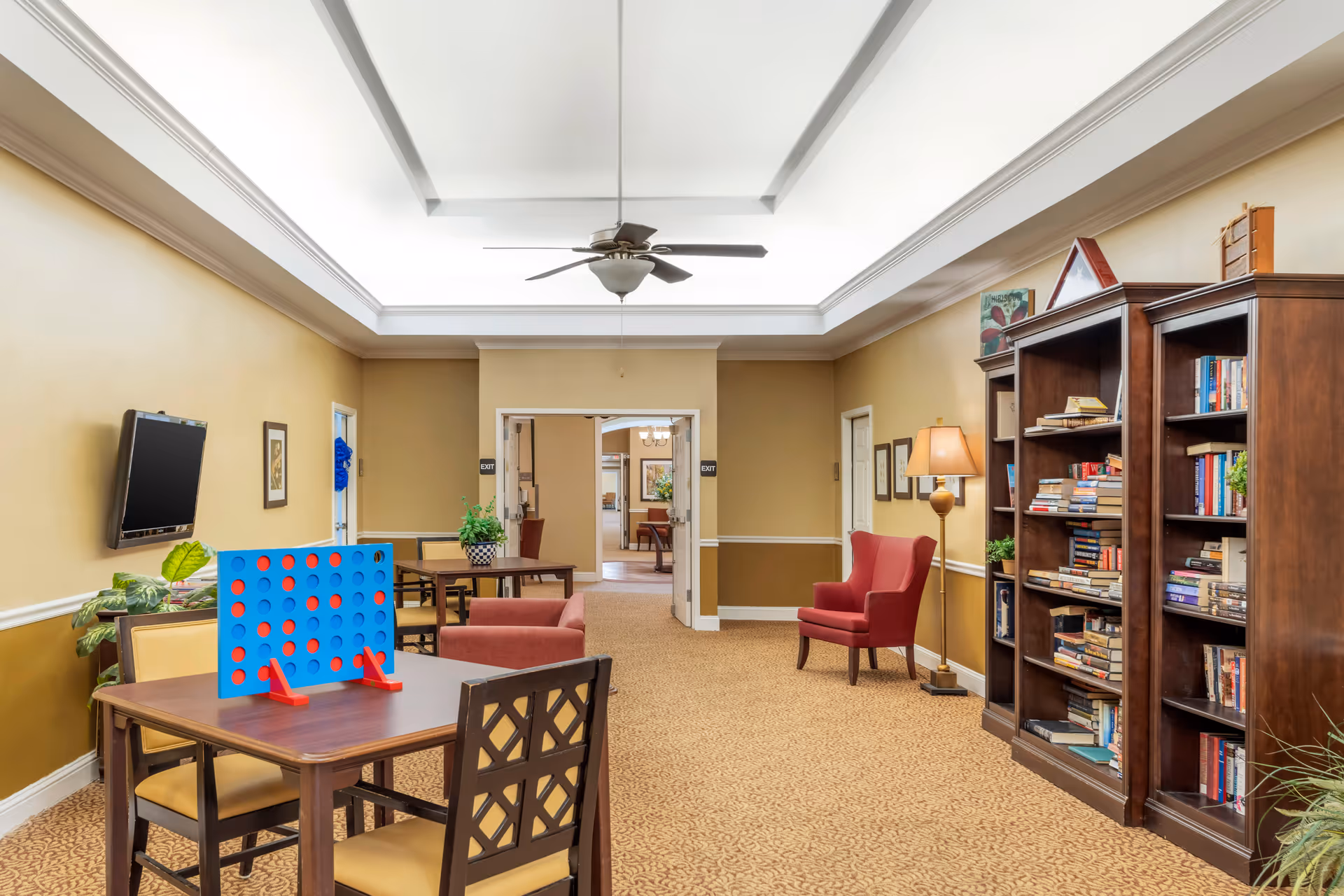 Bright lounge area with ceiling fan, bookshelves, game table, and comfortable seating.
