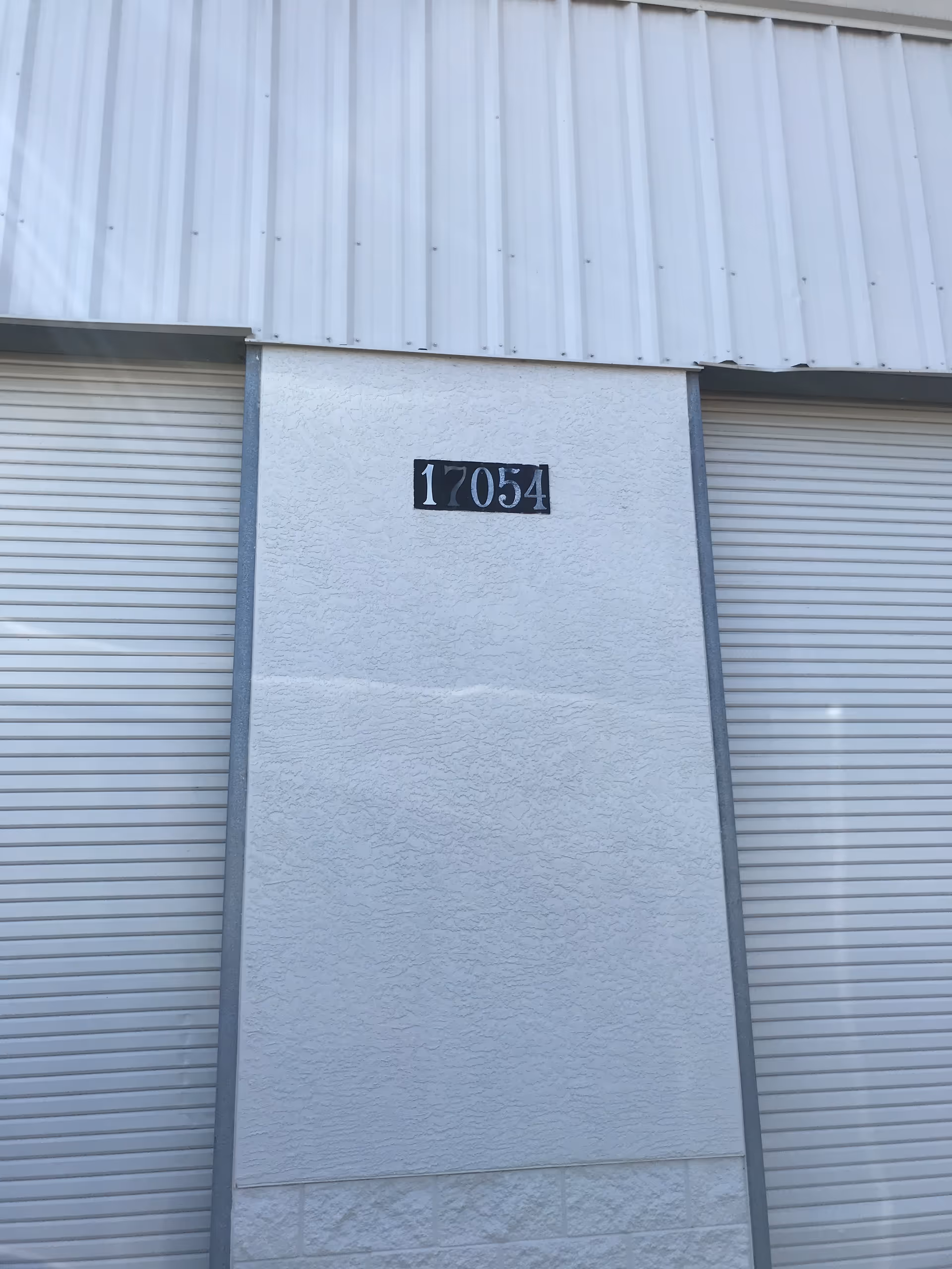 Exterior wall with a vertical column and closed metal roll-up doors, building number 17054.