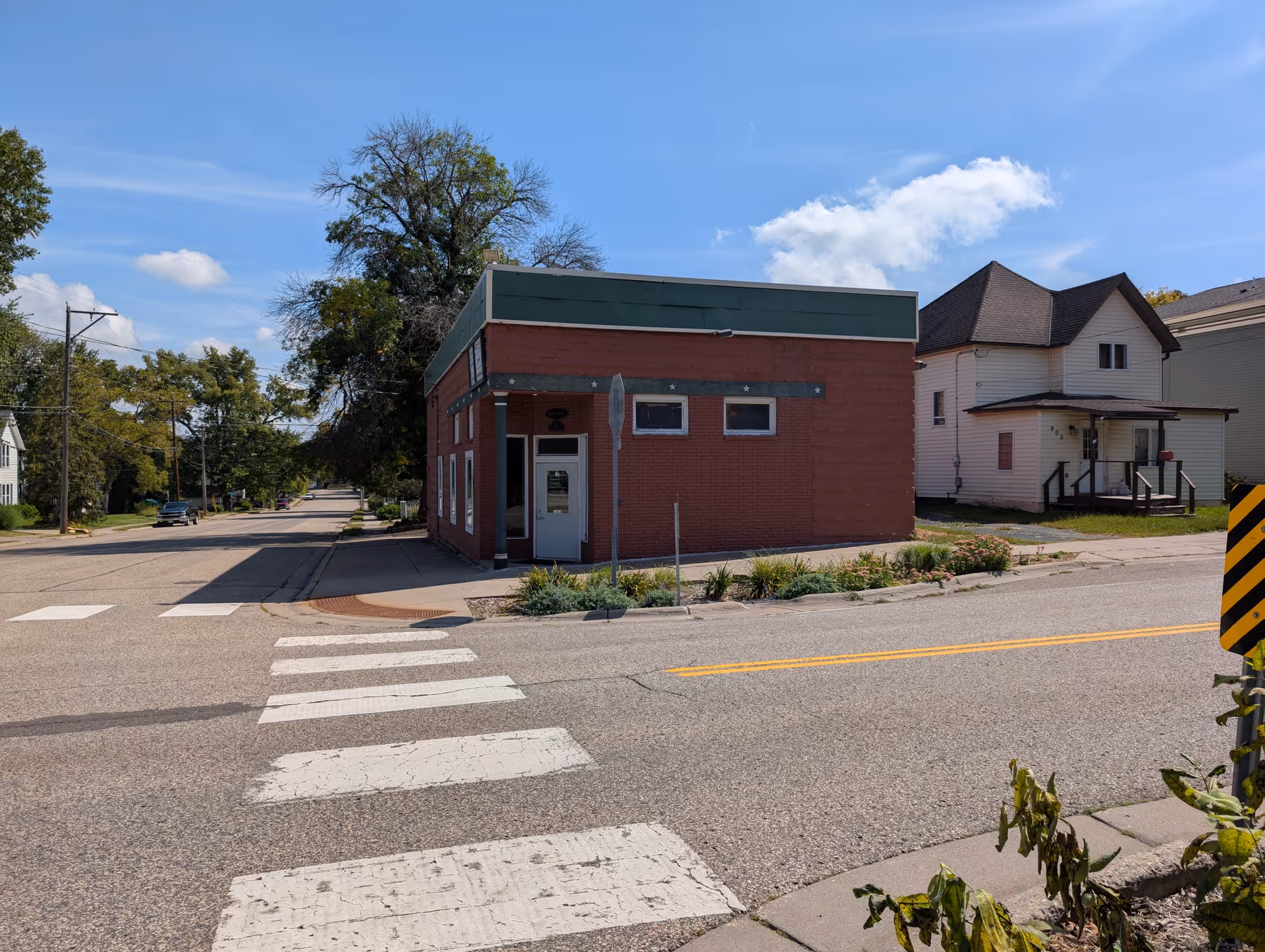 Small brick building with a green roof on a quiet street corner.