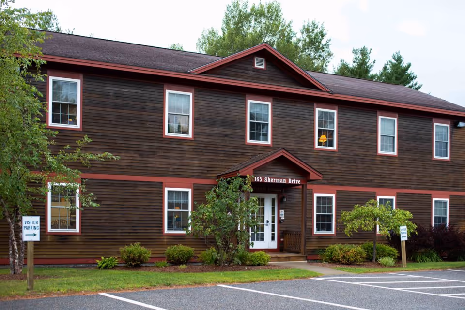Brown wooden two-story building with red trim and central entrance, parking spaces visible in front.