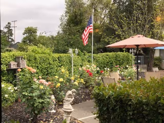 Outdoor garden patio with flower beds, an American flag, seating, and a pink patio umbrella.