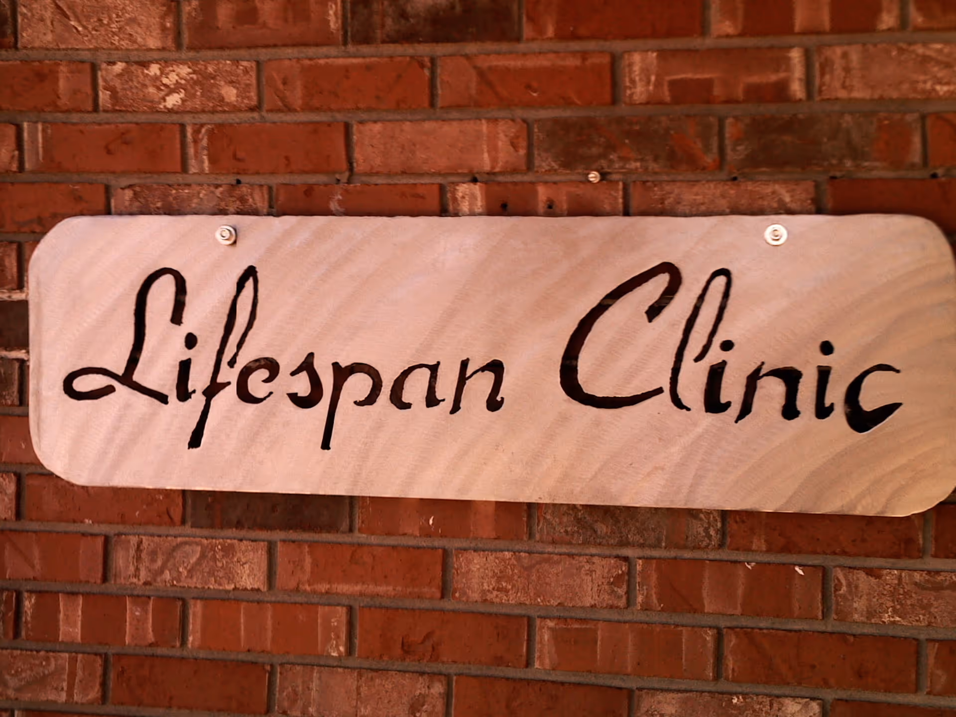 Wooden sign reading Lifespan Clinic mounted on brick exterior wall.