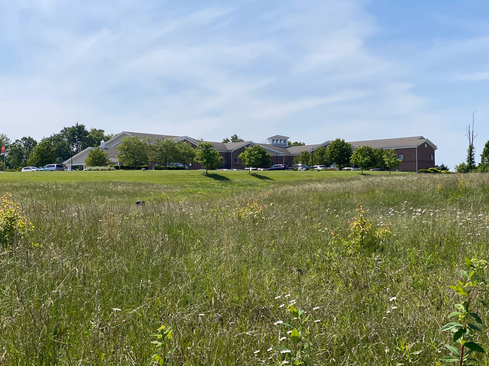 Single-story senior facility with brick exterior, surrounding lawn, and visible parking lot.