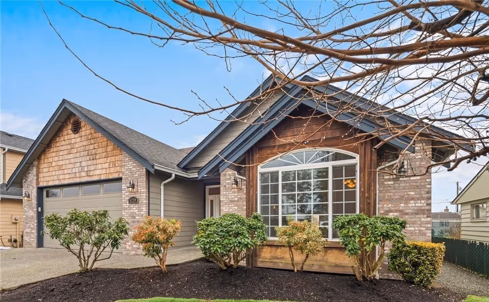 Front view of a single-story brick home with a large front window and shrubs.