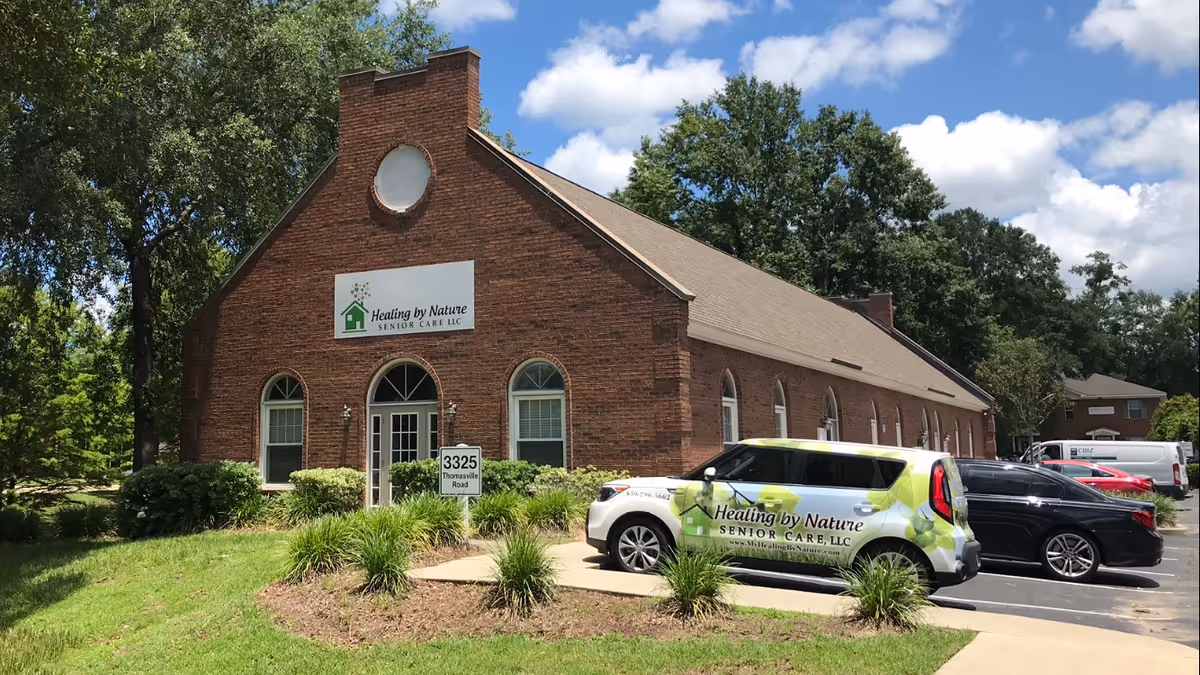 Brick facility exterior with Healing by Nature Senior Care sign and parked cars outside