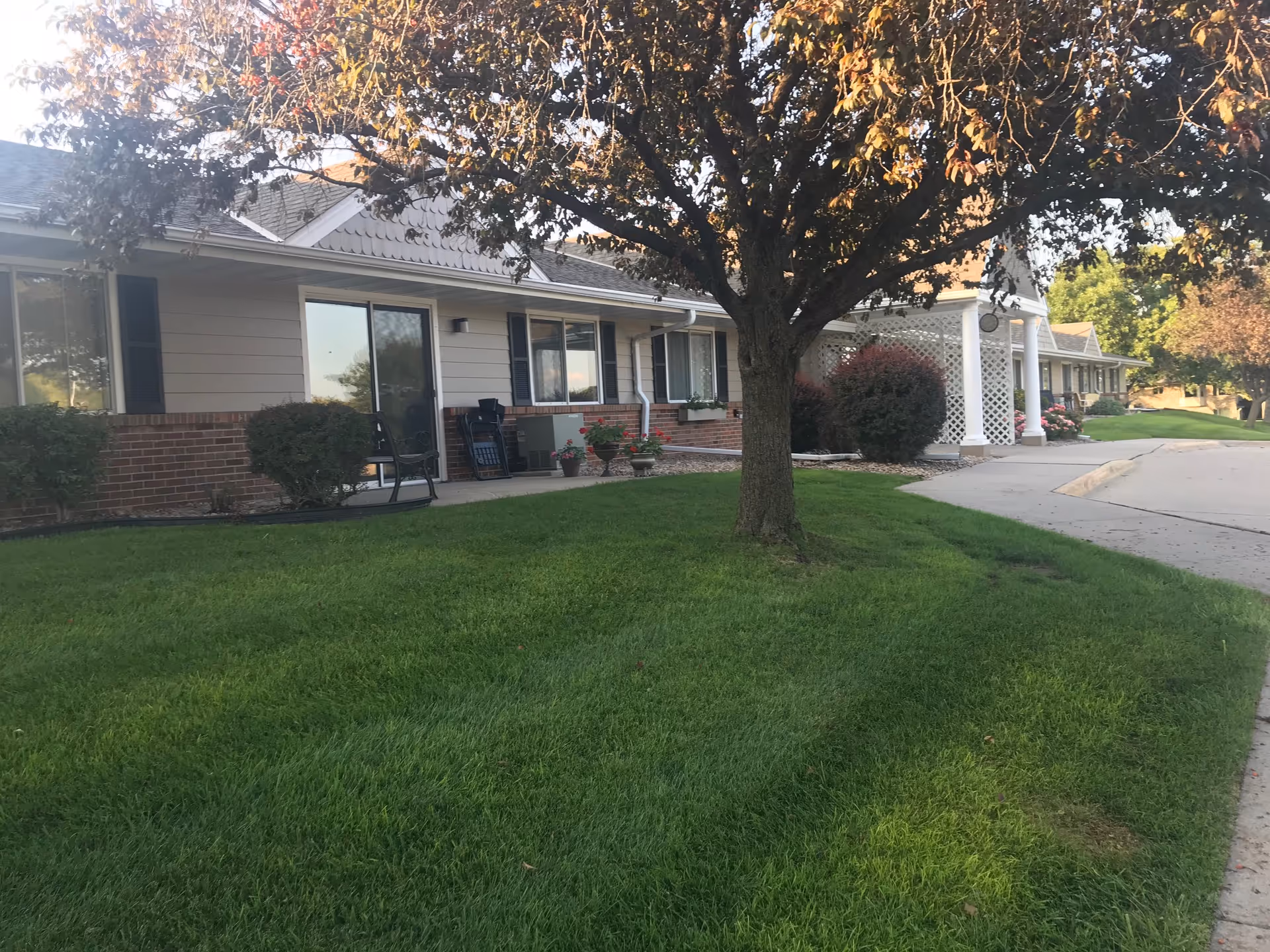 A single-story senior living facility exterior with green lawn and a tree in front.