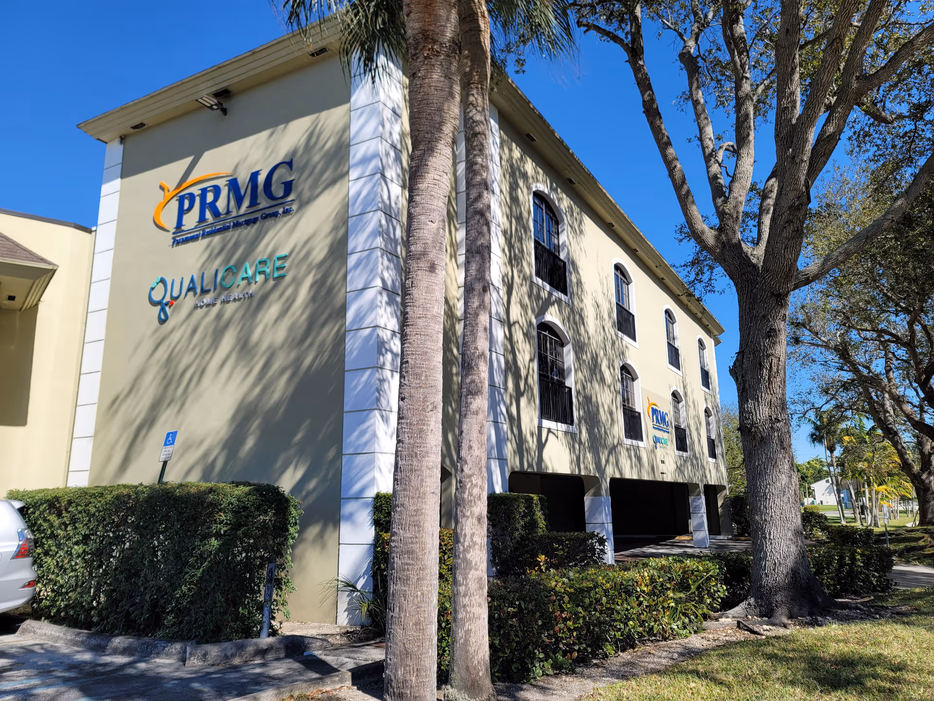 Exterior view of a beige multi-story building with Qualicare signage and palm trees.