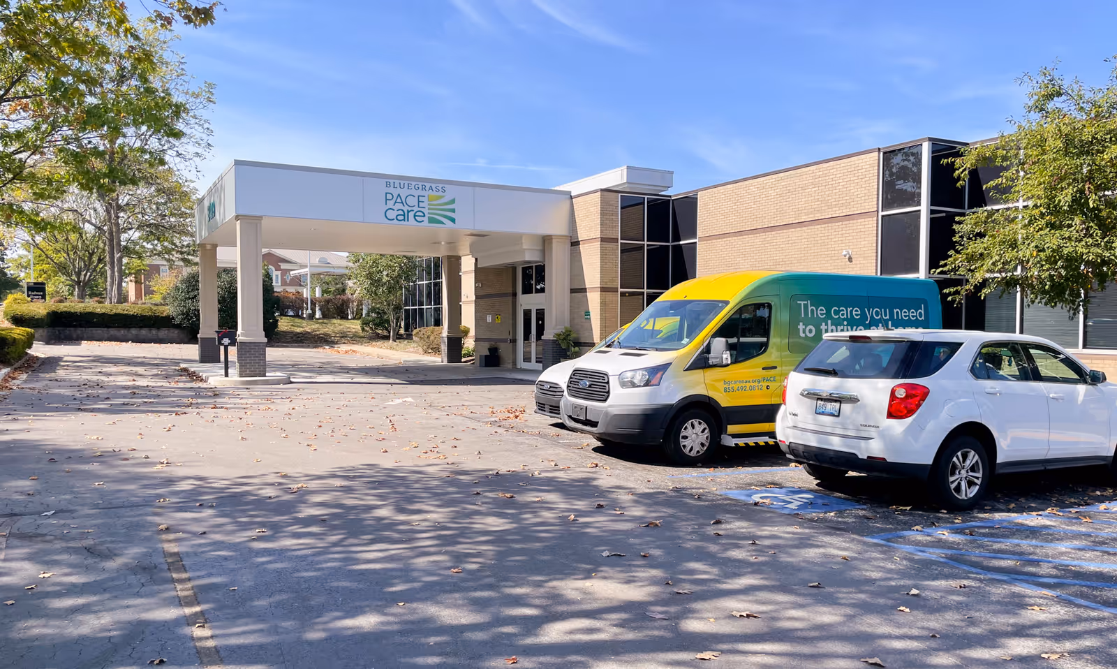 Exterior view of Bluegrass PACE Care facility with entrance canopy and parked vans.