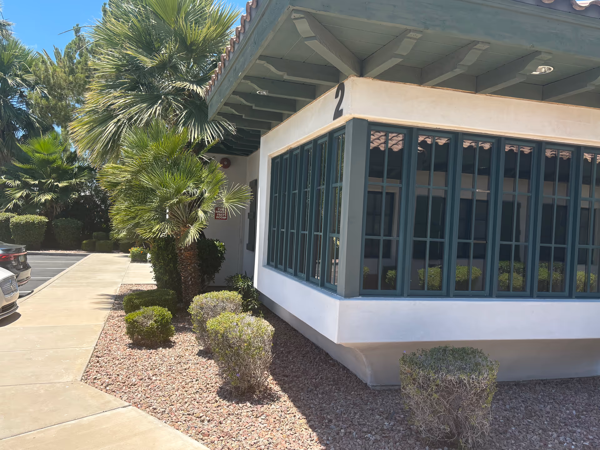 Exterior of a single-story facility with large windows, palm trees, and desert landscaping.