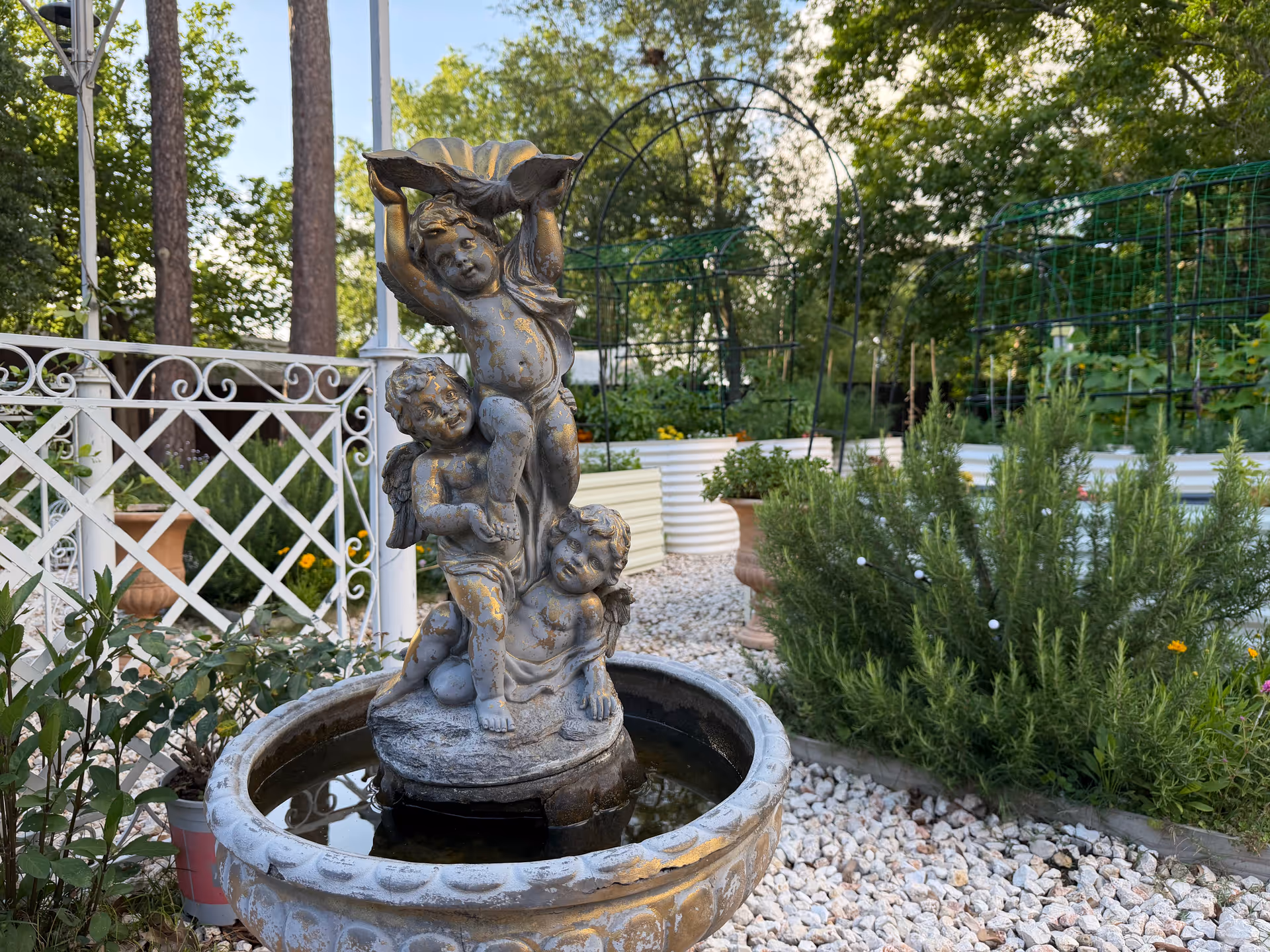 Stone statue fountain with three cherub-like figures in a garden.