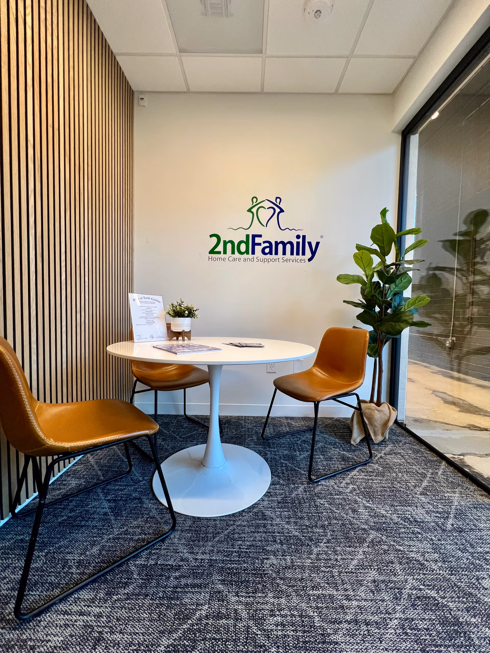 Interior waiting area with a white table, brown chairs, and a 2ndFamily logo on the wall.