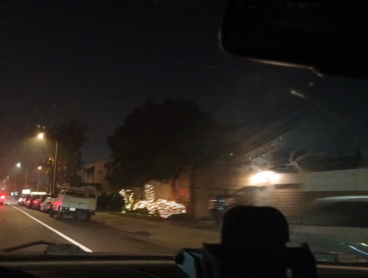 Nighttime street view with parked cars and festive lights along a building.