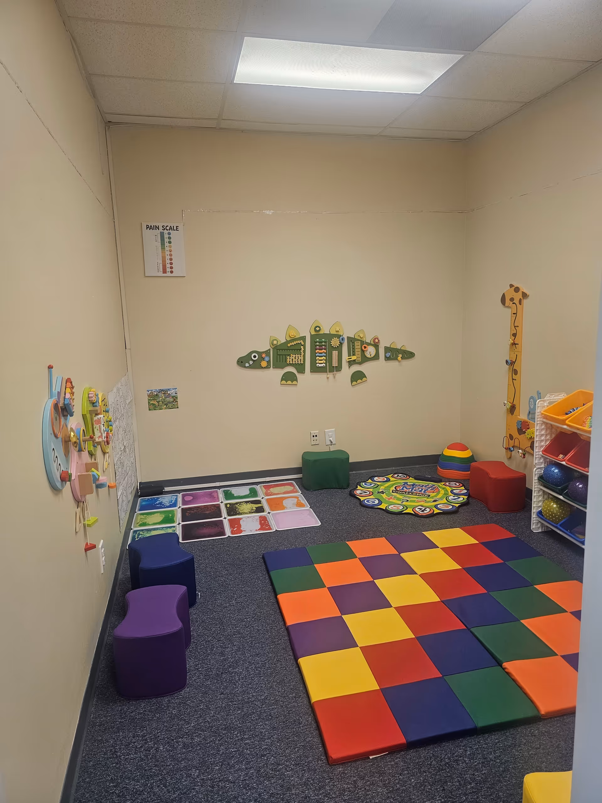 Colorful padded play area with mats, shelves, and wall decorations in a small indoor room.