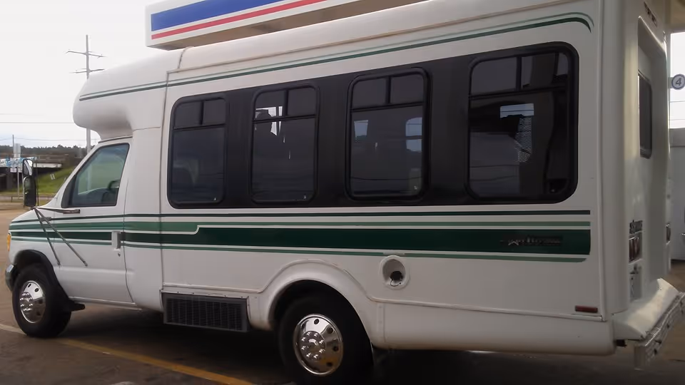 White shuttle bus with green stripes parked outdoors, rear and side windows visible.