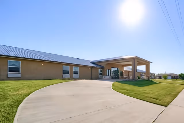 Wide view of a single-story senior living facility exterior with a curved driveway and entrance.