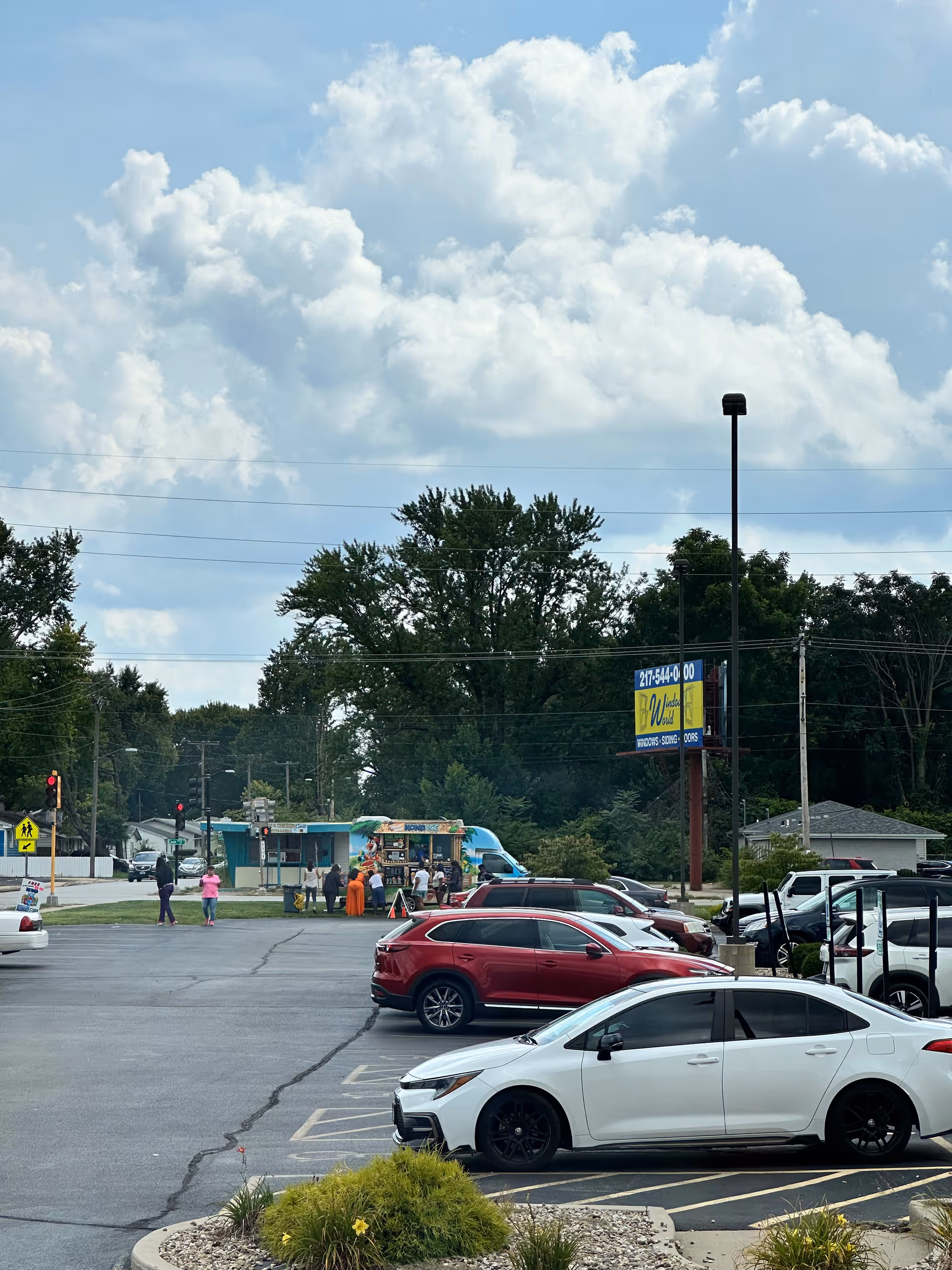 Parking lot outside a facility with several cars, a blue food truck, and distant pedestrians.