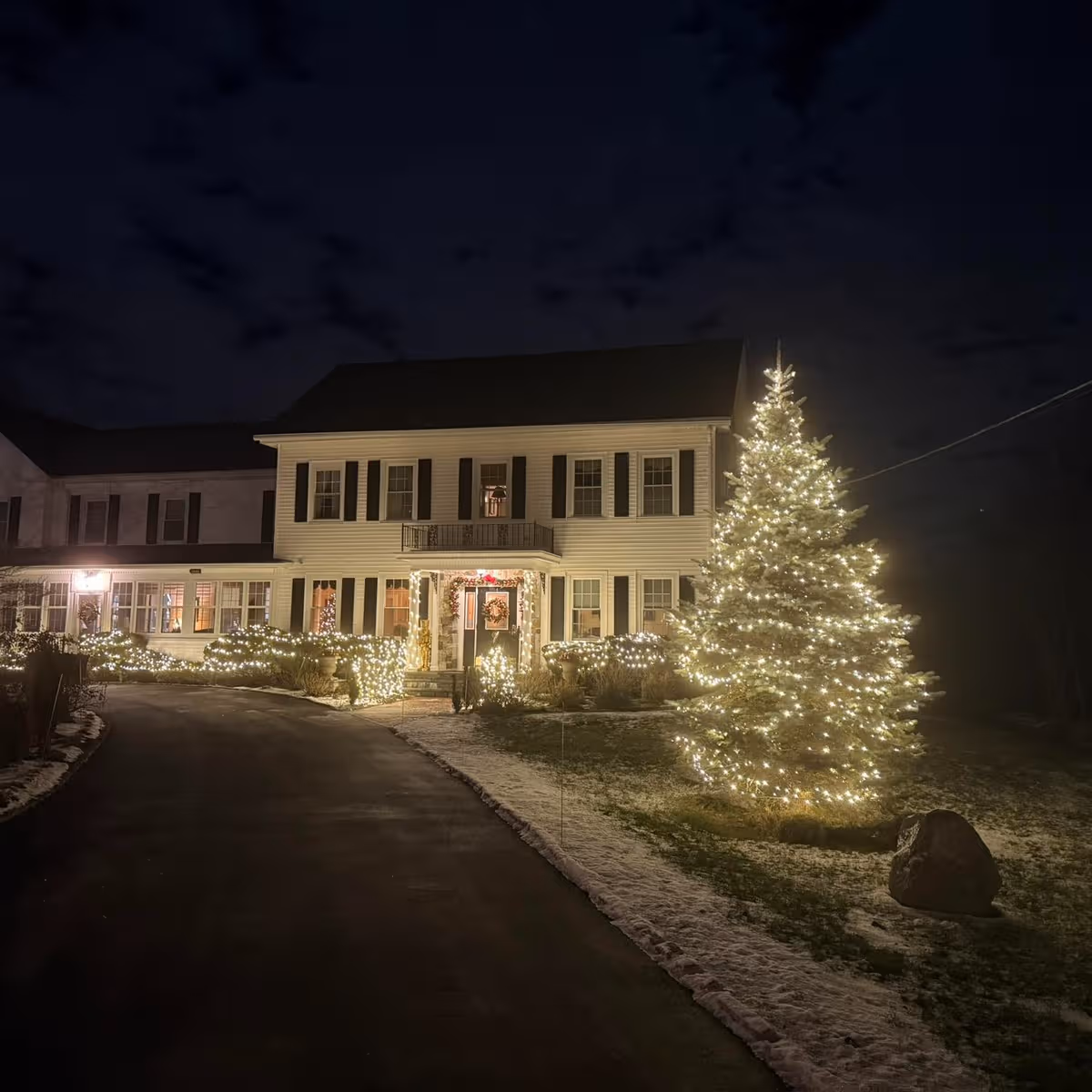 Night exterior view of Charlton Manor Rest Home with illuminated Christmas tree and front lawn lights.