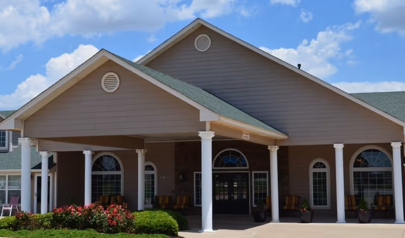 Front view of a beige senior living facility with covered entrance and white columns.