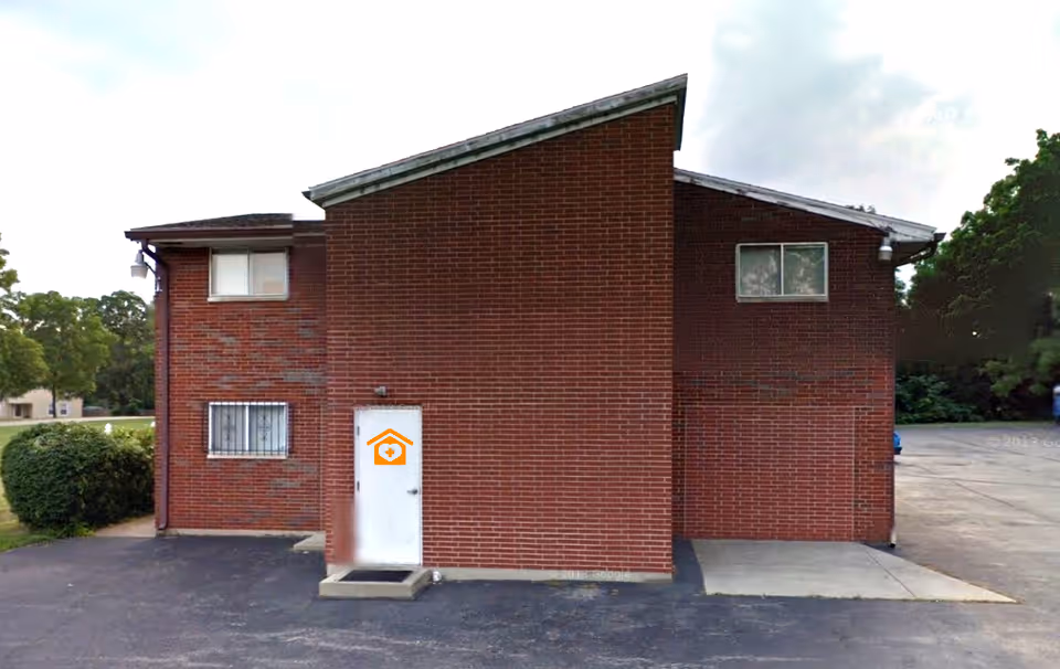 Two-story brick building with a white door featuring an orange house logo.