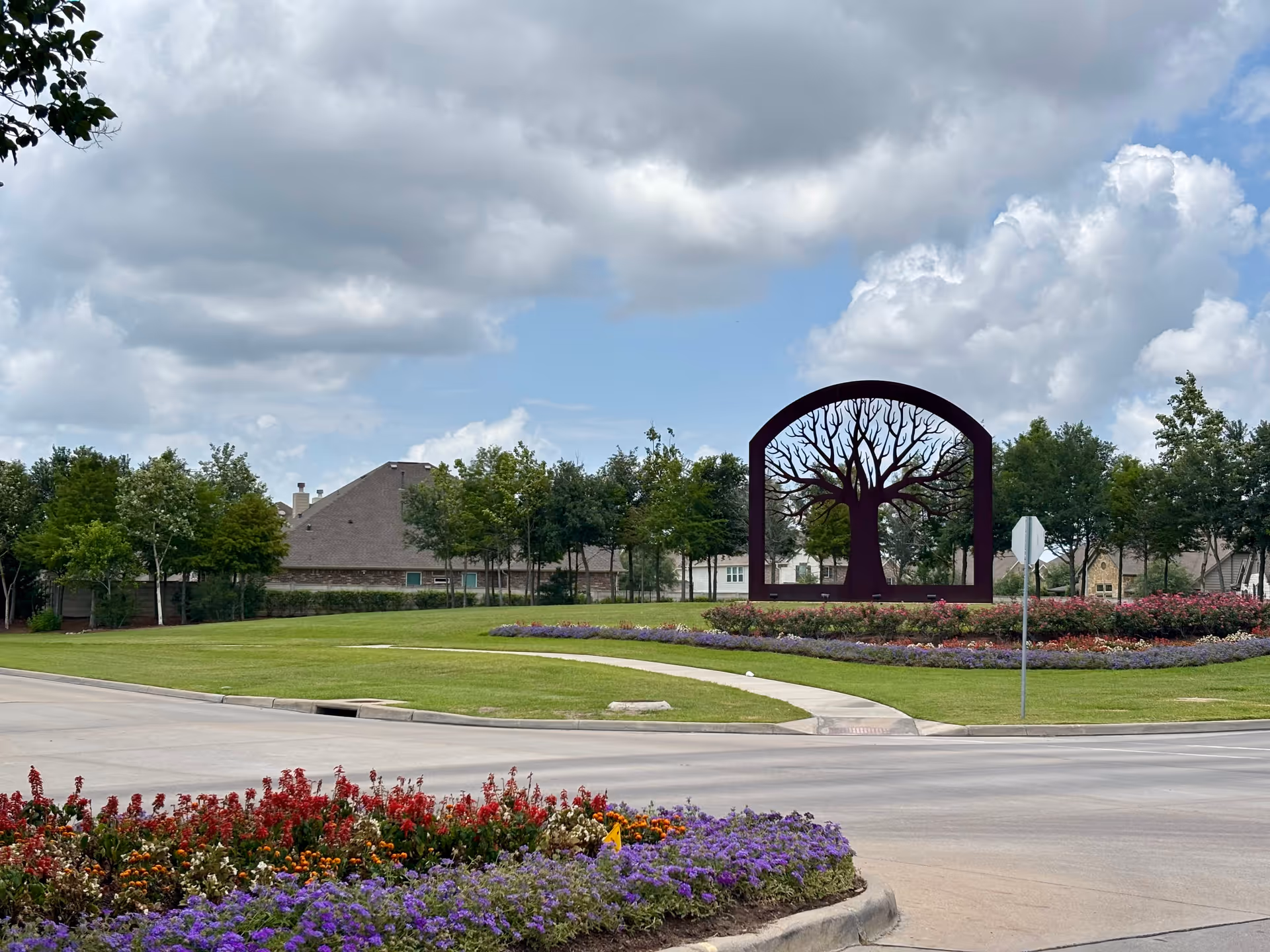 Roundabout with flower beds and a large arch-tree sculpture near a building