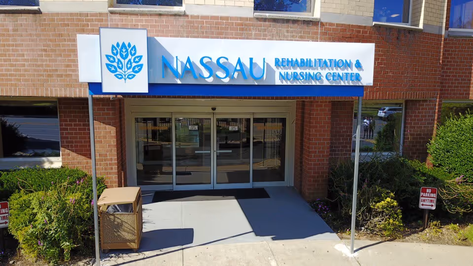Exterior entrance of Nassau Rehabilitation & Nursing Center with glass doors and signage.