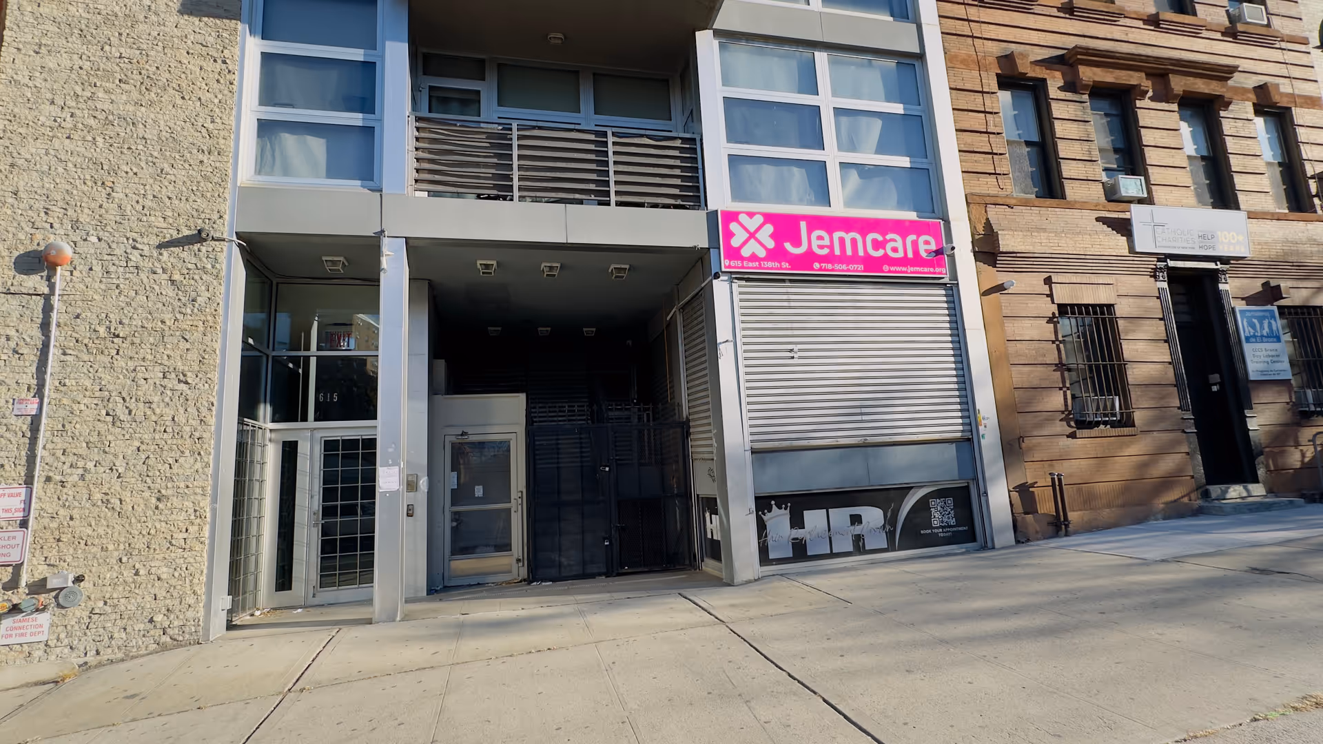 Urban building facade featuring a pink Jemcare sign and a gated entrance.