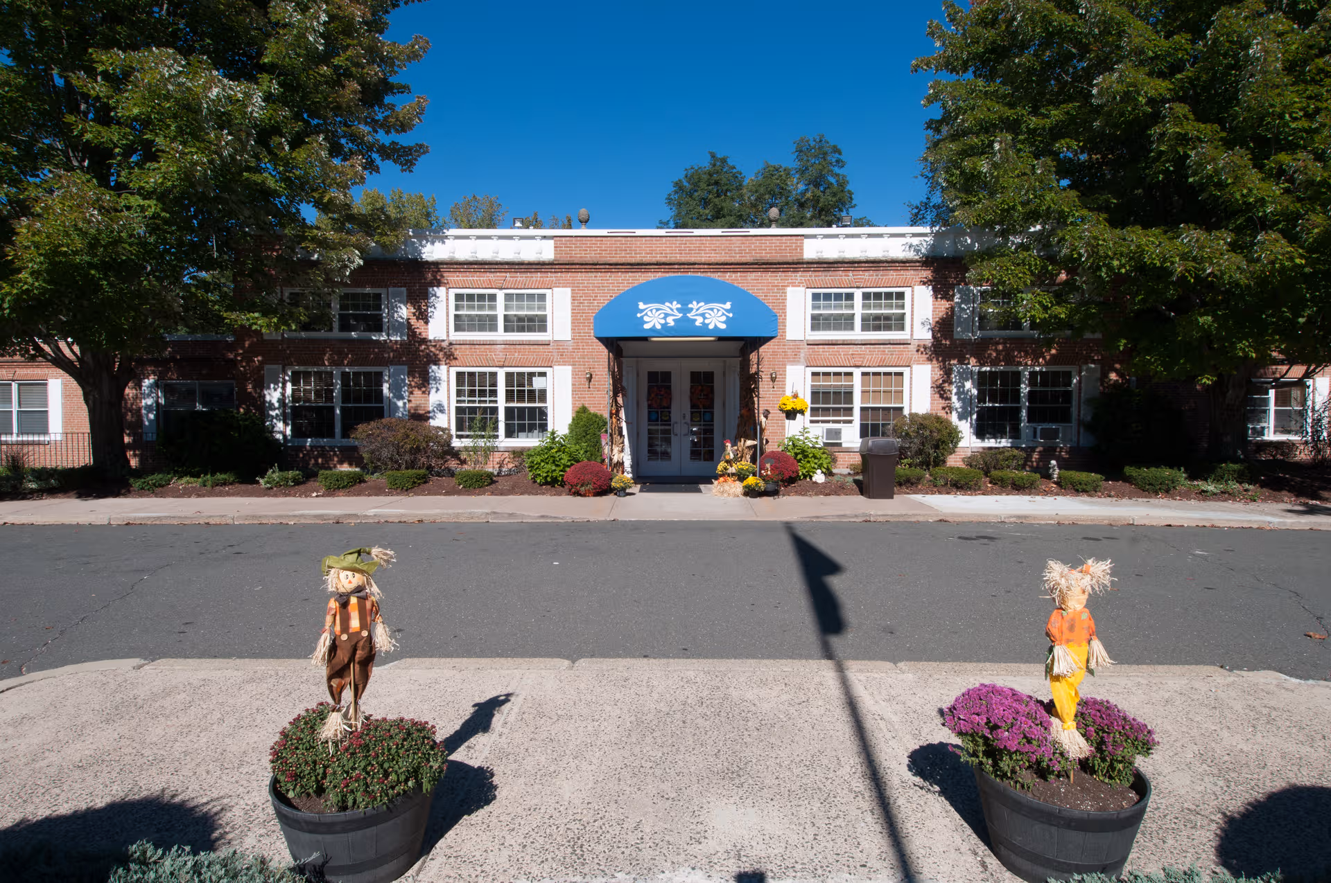 Brick senior living facility exterior with blue entrance awning and decorative planters.