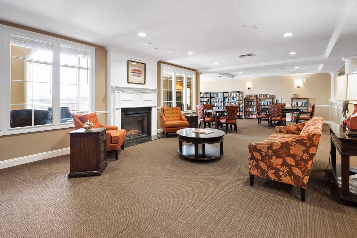 A spacious senior lounge with a fireplace, bookshelves, and orange chairs.