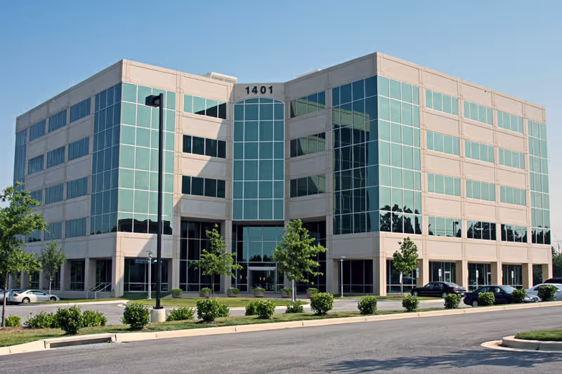 Modern glass-and-concrete office building with a central rounded tower and landscaped frontage.