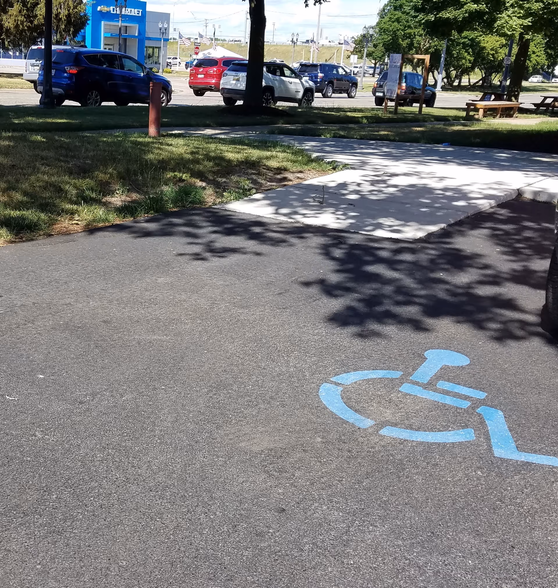 Parking lot and sidewalk with handicap symbol, benches, and trees outdoors.