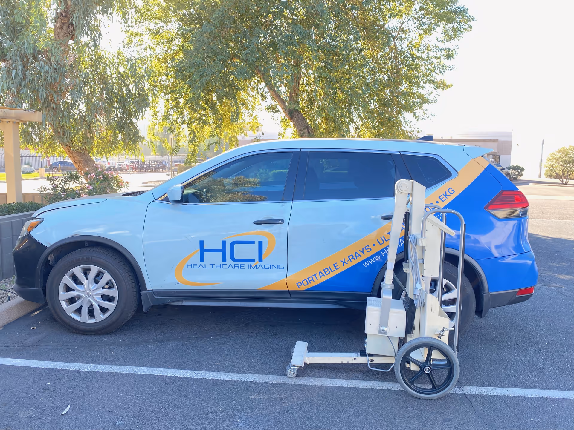 Light blue HCI Healthcare Imaging van parked beside a portable X-ray machine outdoors.