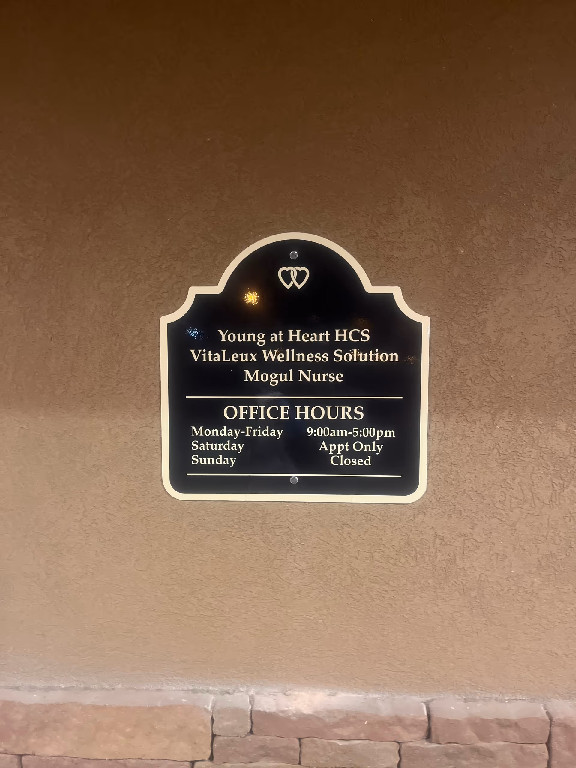 Black plaque with office hours mounted on brown exterior wall.