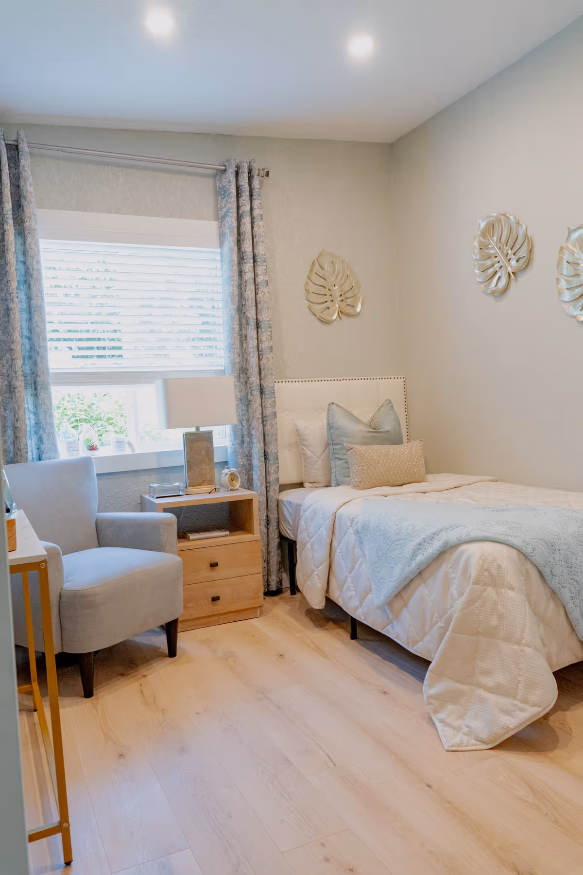 Cozy bedroom with a bed, chair, nightstand, window, and light blue decor.