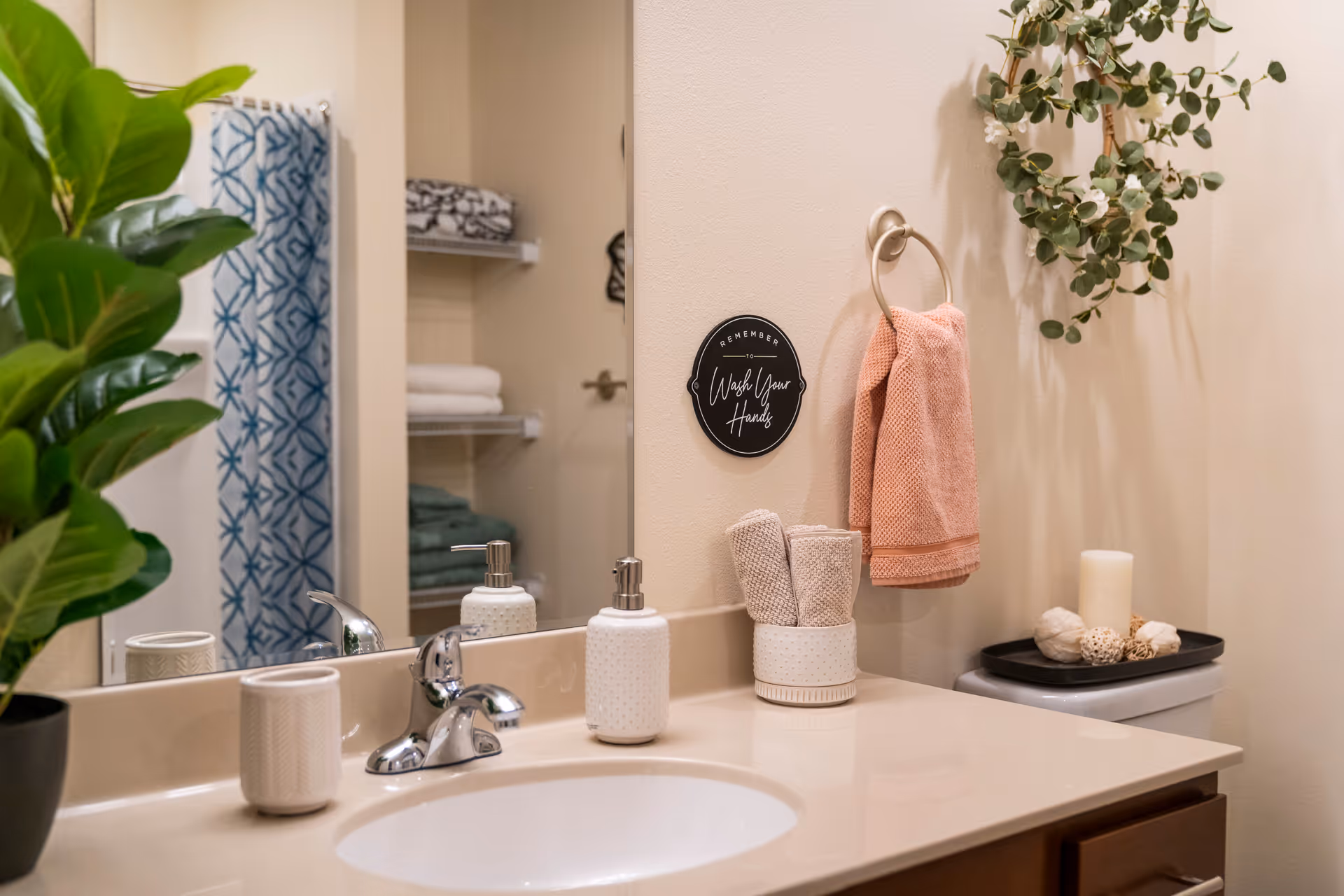 Clean bathroom vanity with sink, mirror, towels, plant, and hand wash station.