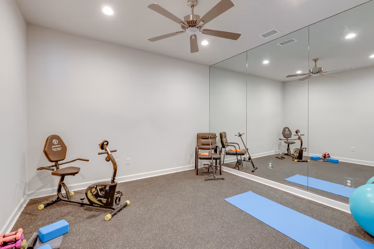Small indoor exercise room with a stationary bike, yoga mats, and a mirrored wall.