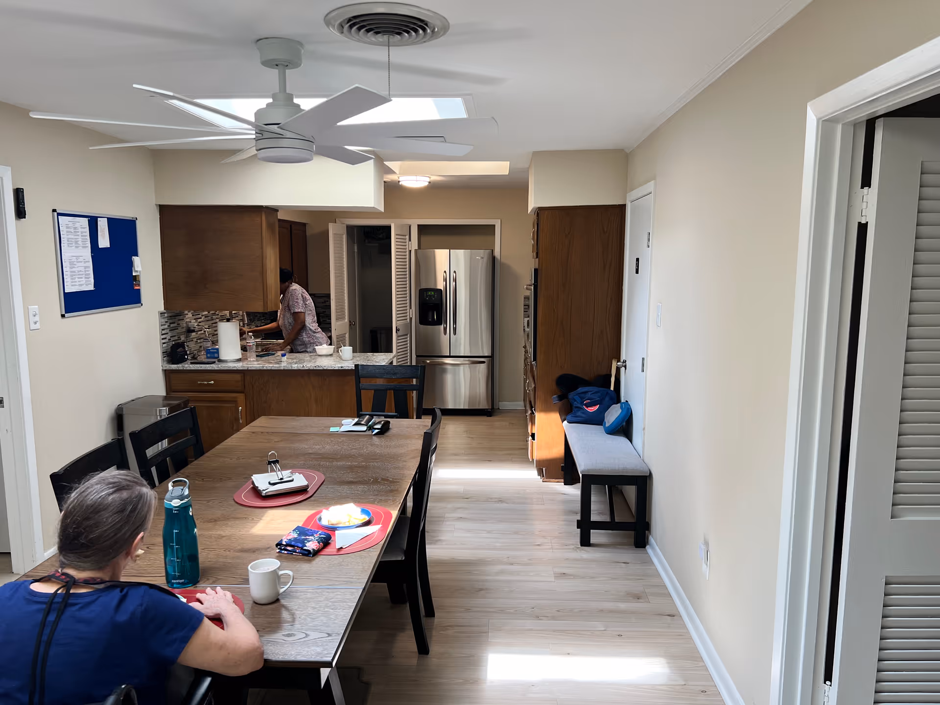 Long dining table in a senior living dining area with a kitchen visible in the background.