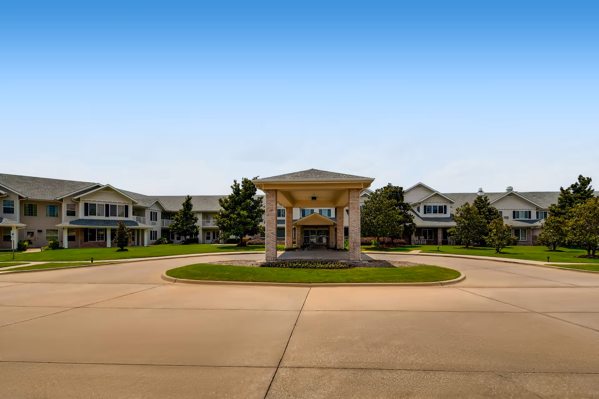 Front entrance of a two-story senior living community with a covered porte-cochere and circular driveway.