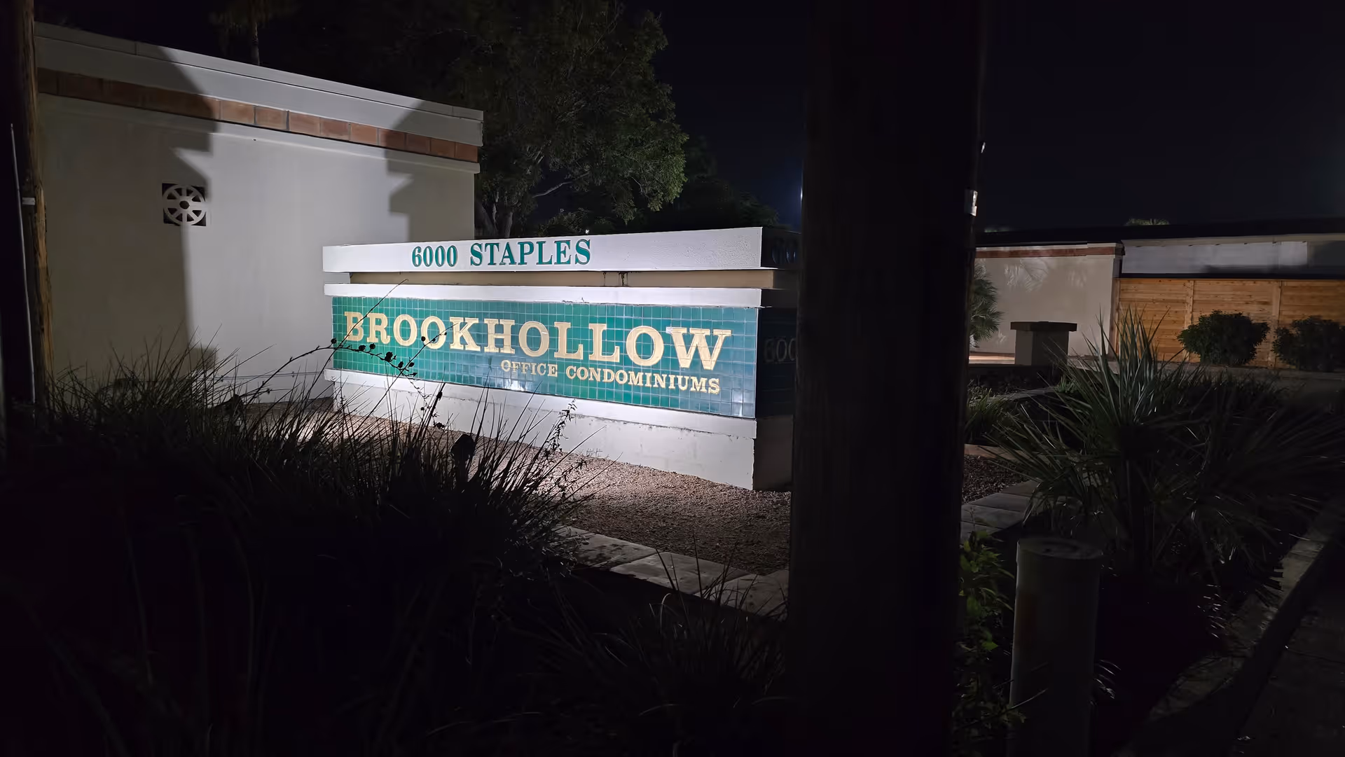 Nighttime exterior with a lit sign reading Brookhollow Office Condominiums amid desert landscaping.