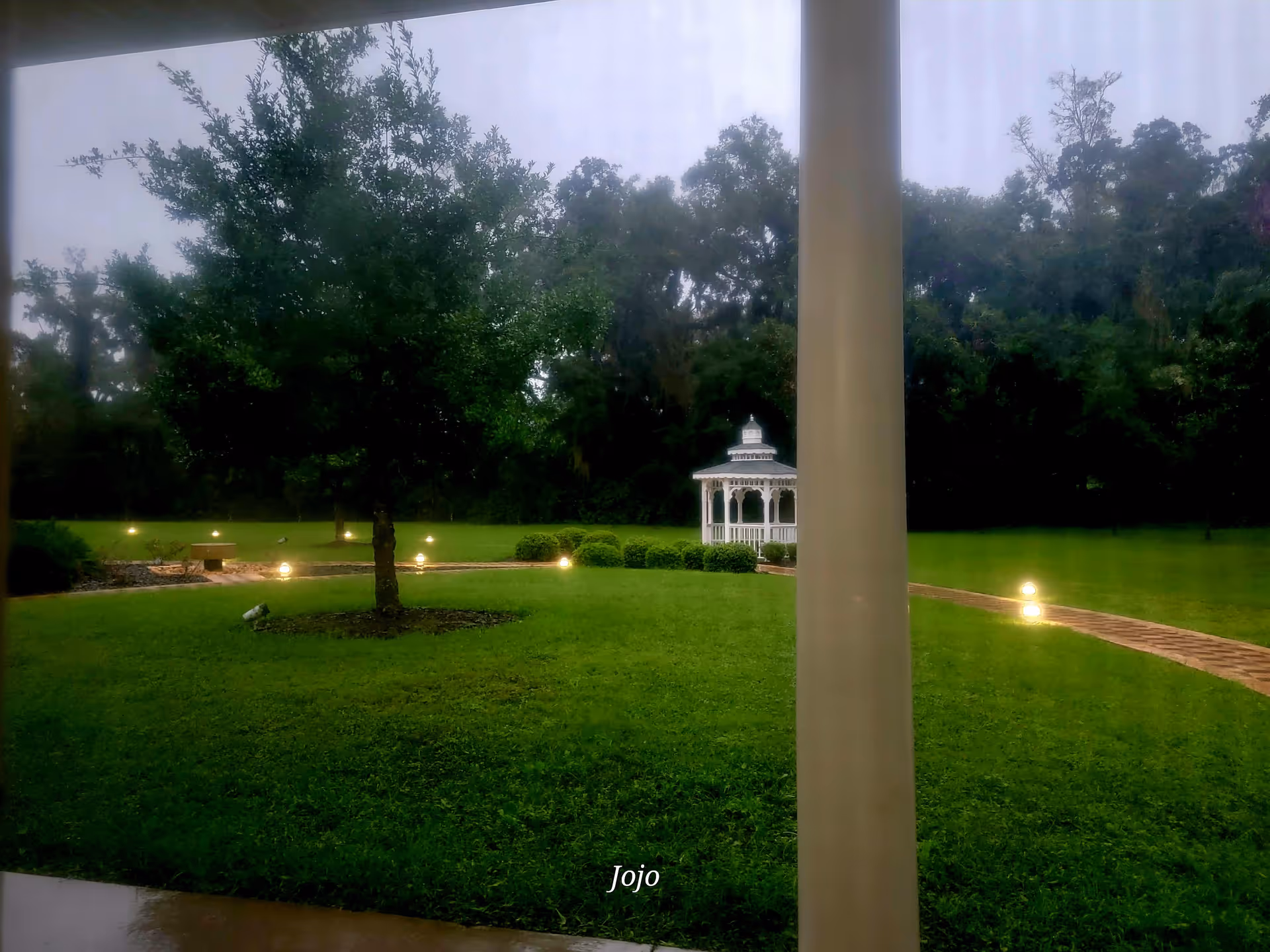 View from a porch shows green lawn, white gazebo, and curved path.