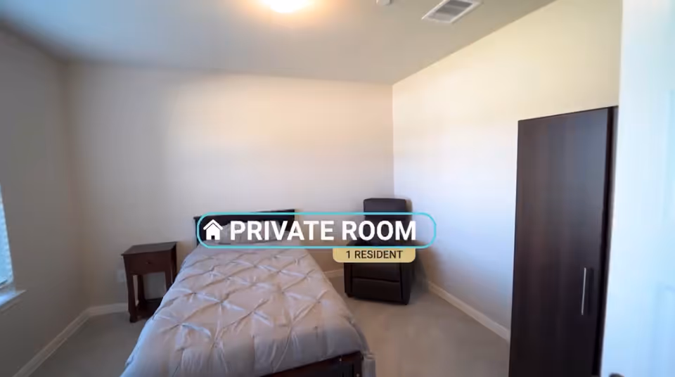 A private bedroom with a bed, nightstand, chair, and wardrobe.