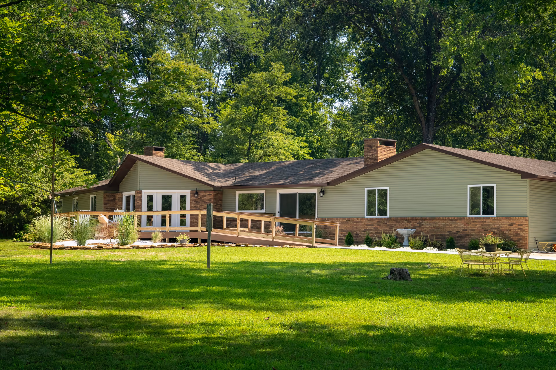 Single-story senior living facility with ramp, lawn, trees, and outdoor seating.