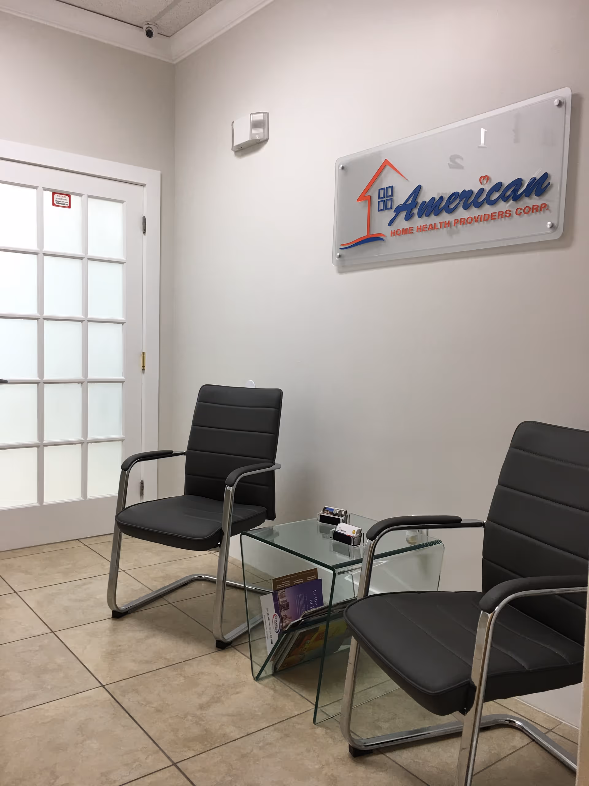 Interior lobby with two black chairs, glass table, magazines, and an American Home Health Providers sign.
