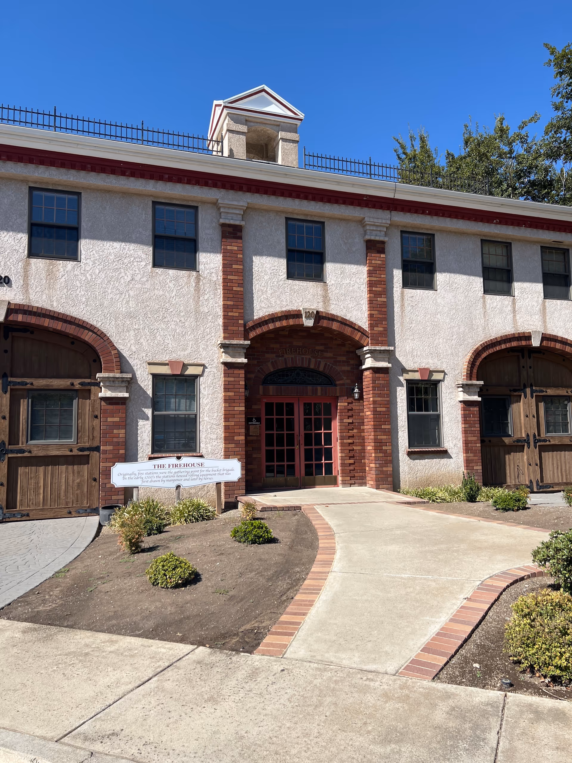 Exterior view of a brick building with arched brick entry and red doors along a walkway.