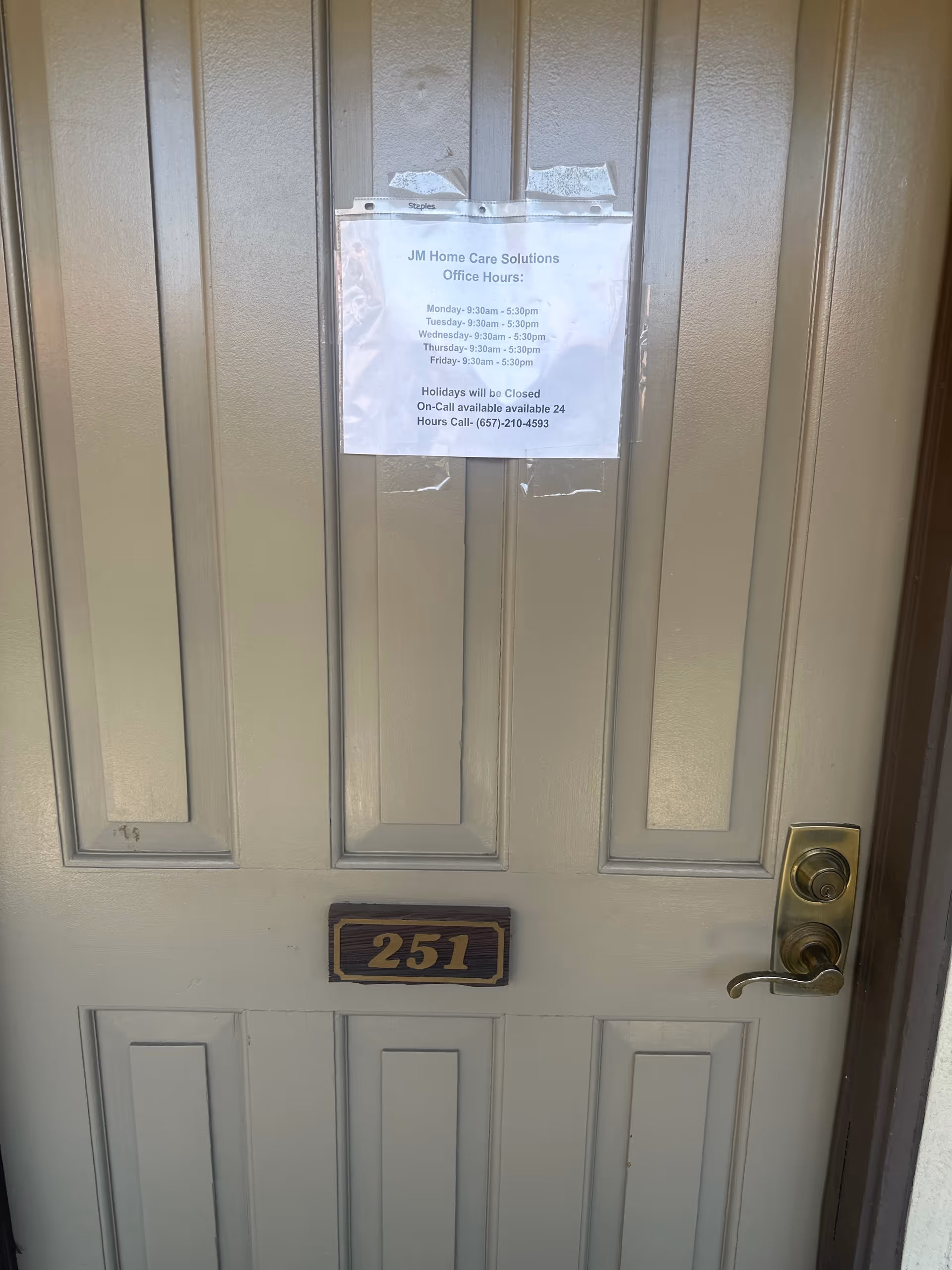 A beige exterior door with a taped JM Home Care Solutions sign and 251 plaque.