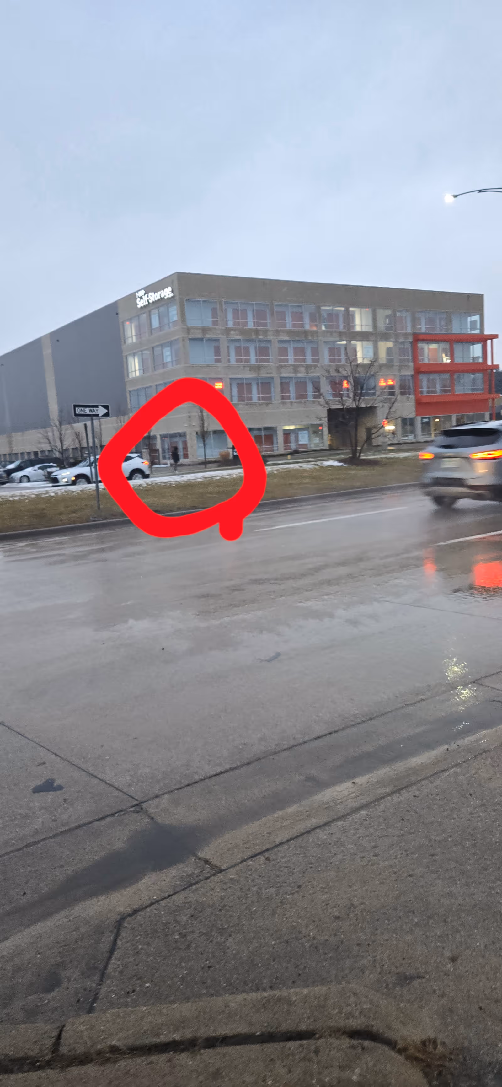 Exterior view of a multi-story facility along a wet street.