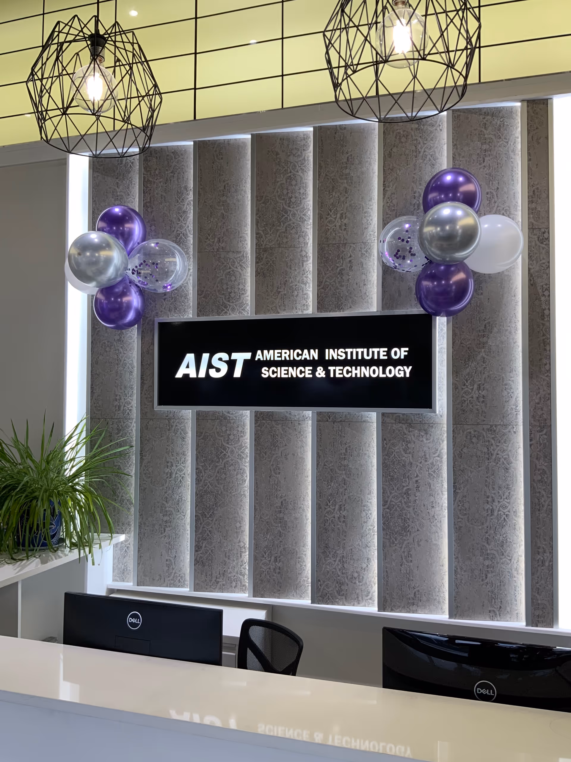 Reception desk with sign, balloons, and decorative wall panels in modern office lobby.