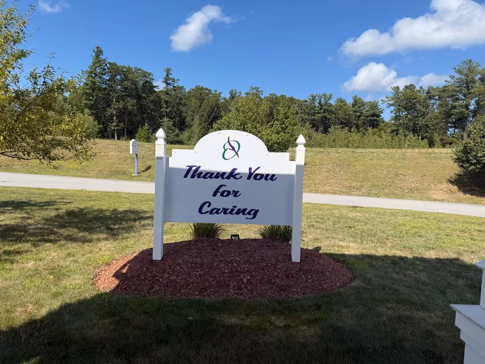 White sign reading 'Thank You for Caring' stands on a mulched bed by grass.
