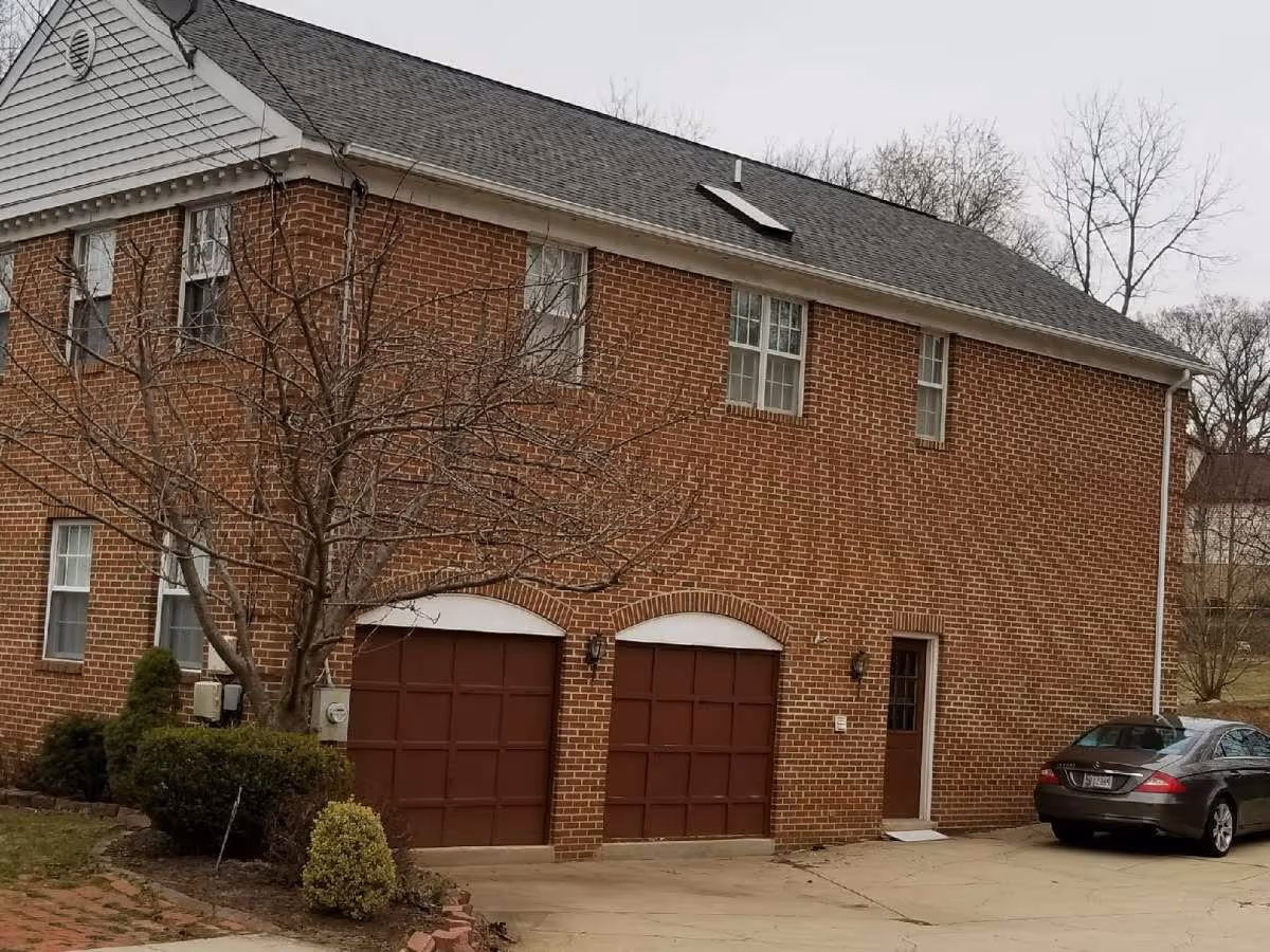Brick two-story building with garage doors, a door, and a car in the driveway.