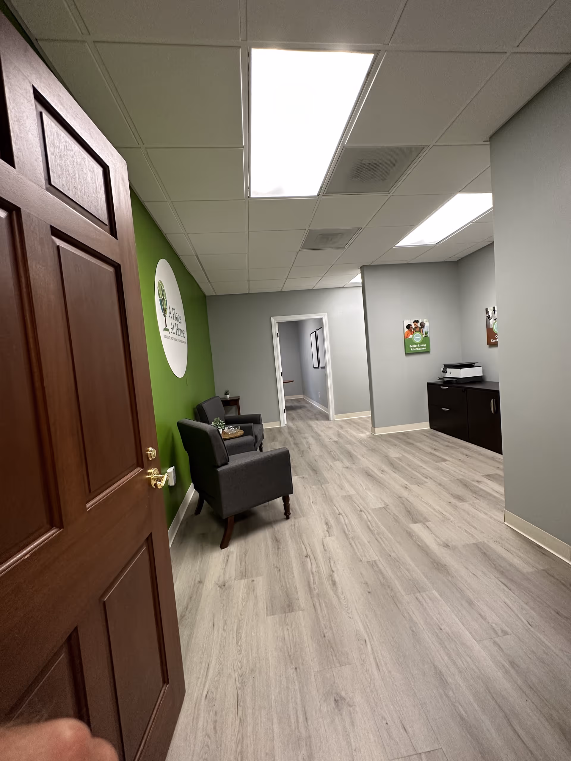 Interior hallway of a senior living facility with seating, green wall, and reception desk.