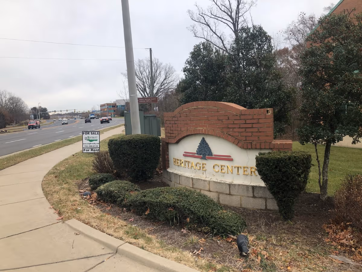Exterior Heritage Center sign with brick arch and trimmed shrubs along a road